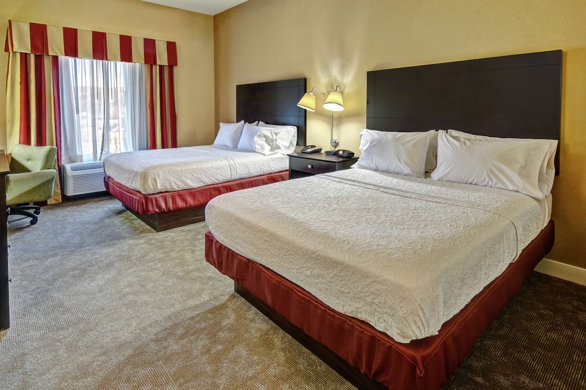 A hotel room with two beds, a desk, a chair, and a window with curtains.