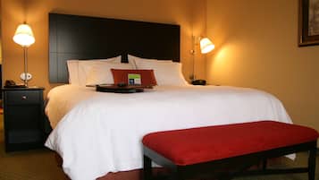 A hotel room with a large bed, two bedside tables, a nightstand, a red bench, and two wall-mounted lamps.