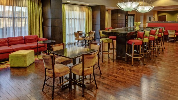 Un hall de hotel con un sofá rojo, una zona de comedor con bar y un mostrador de recepción.