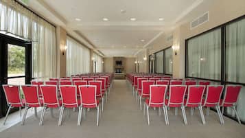 A conference room with rows of red chairs, large windows, and an exit sign.