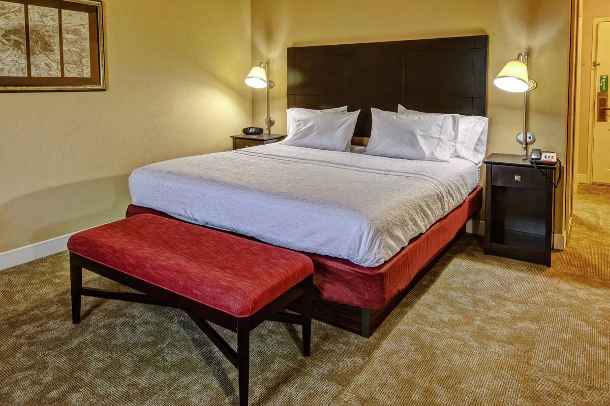 A hotel room with a large bed, two bedside tables, a bench, and a headboard.
