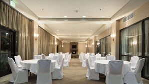 Un salón de conferencias de hotel con mesas redondas, sillas blancas, una chimenea y ventanas grandes.