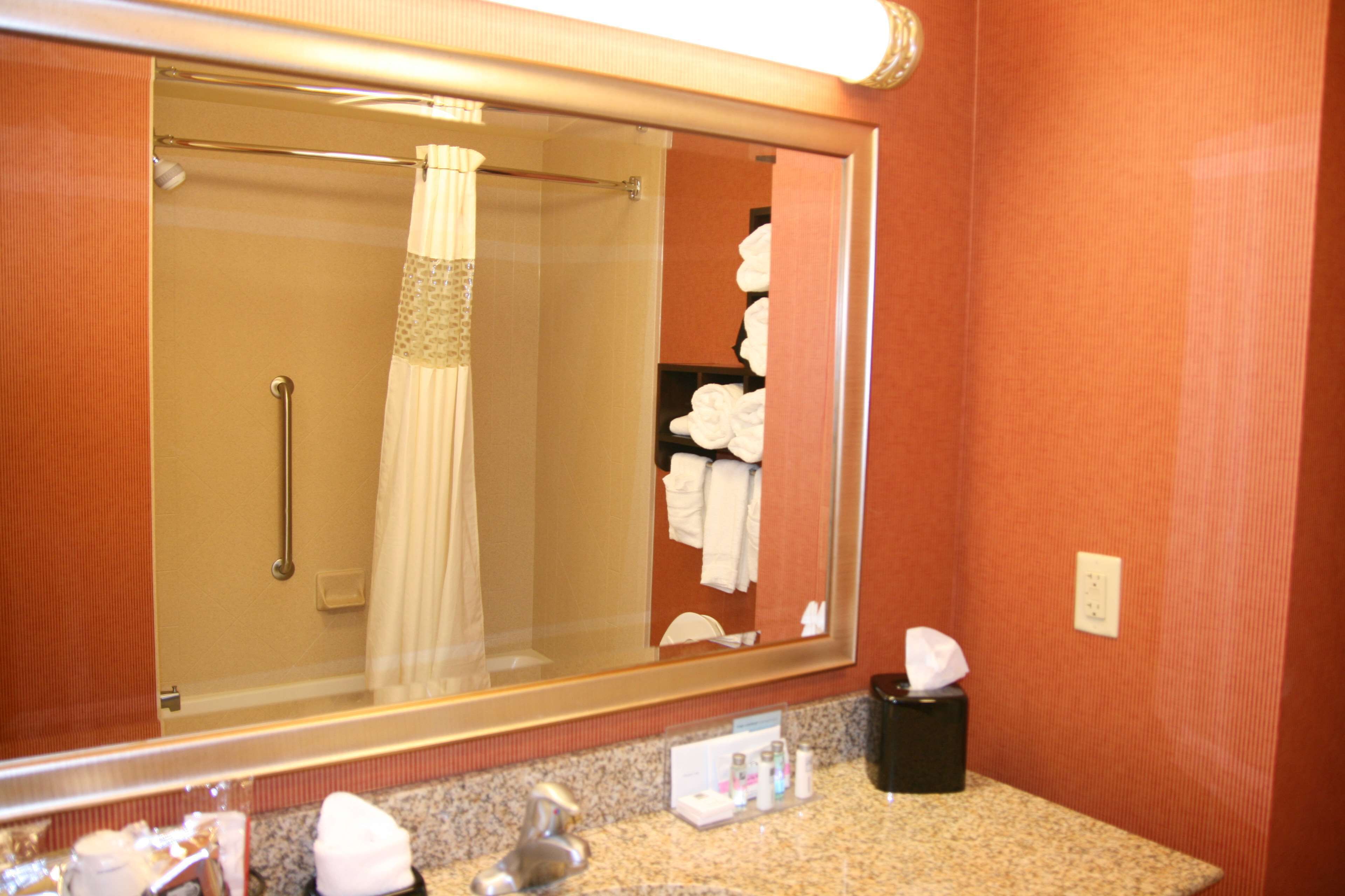 Un baño con un espejo grande, una ducha con puerta de vidrio y un perchero con toallas blancas.