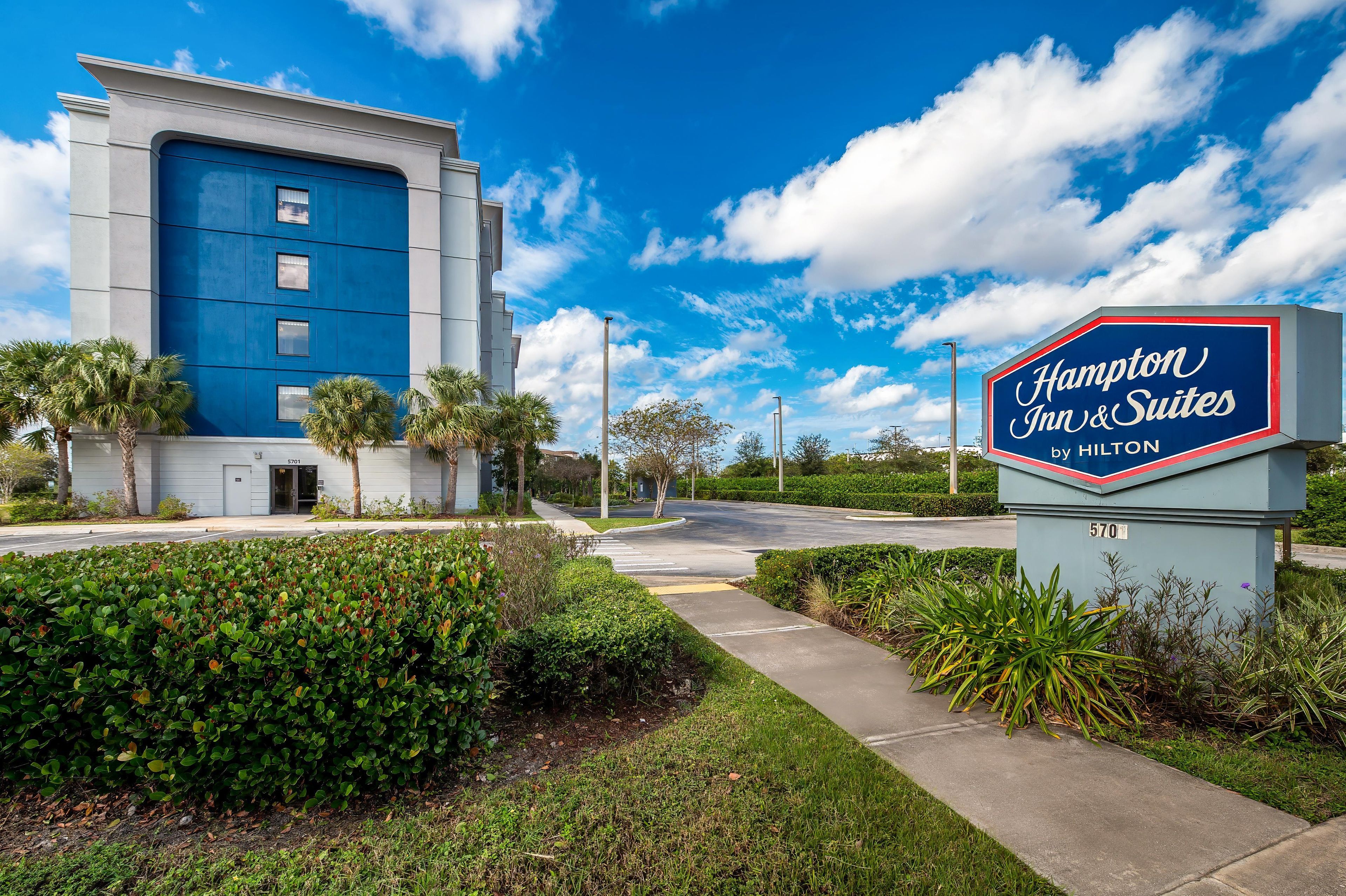 A Hampton Inn & Suites sign with a clear sky and a modern building in the background.
