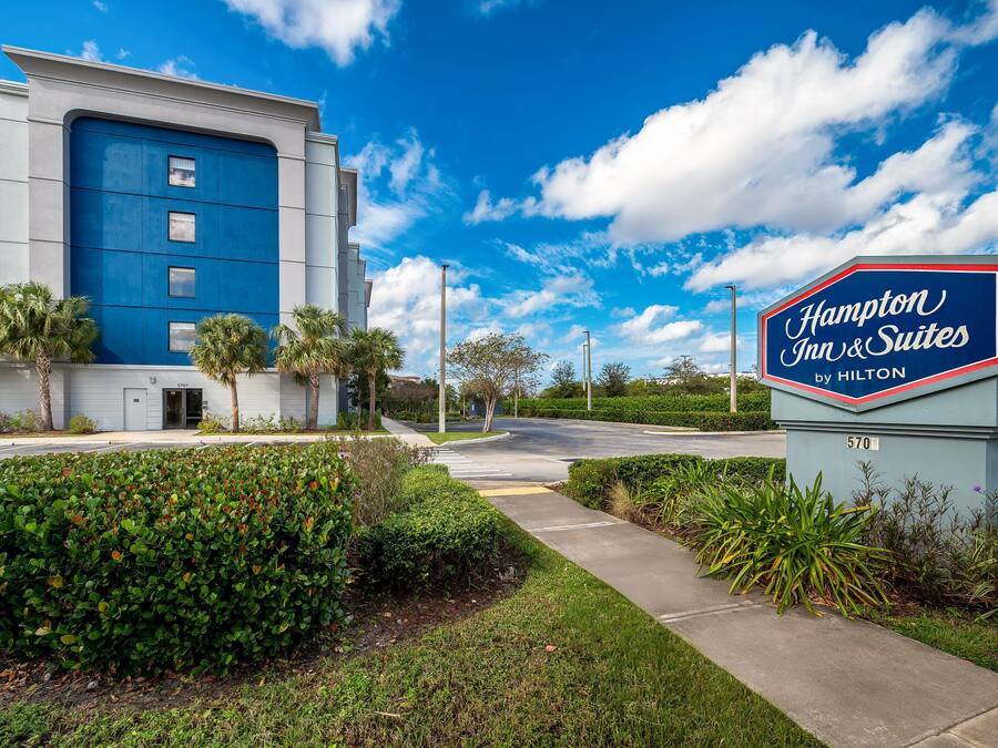 A Hampton Inn & Suites sign with a clear sky and a modern building in the background.