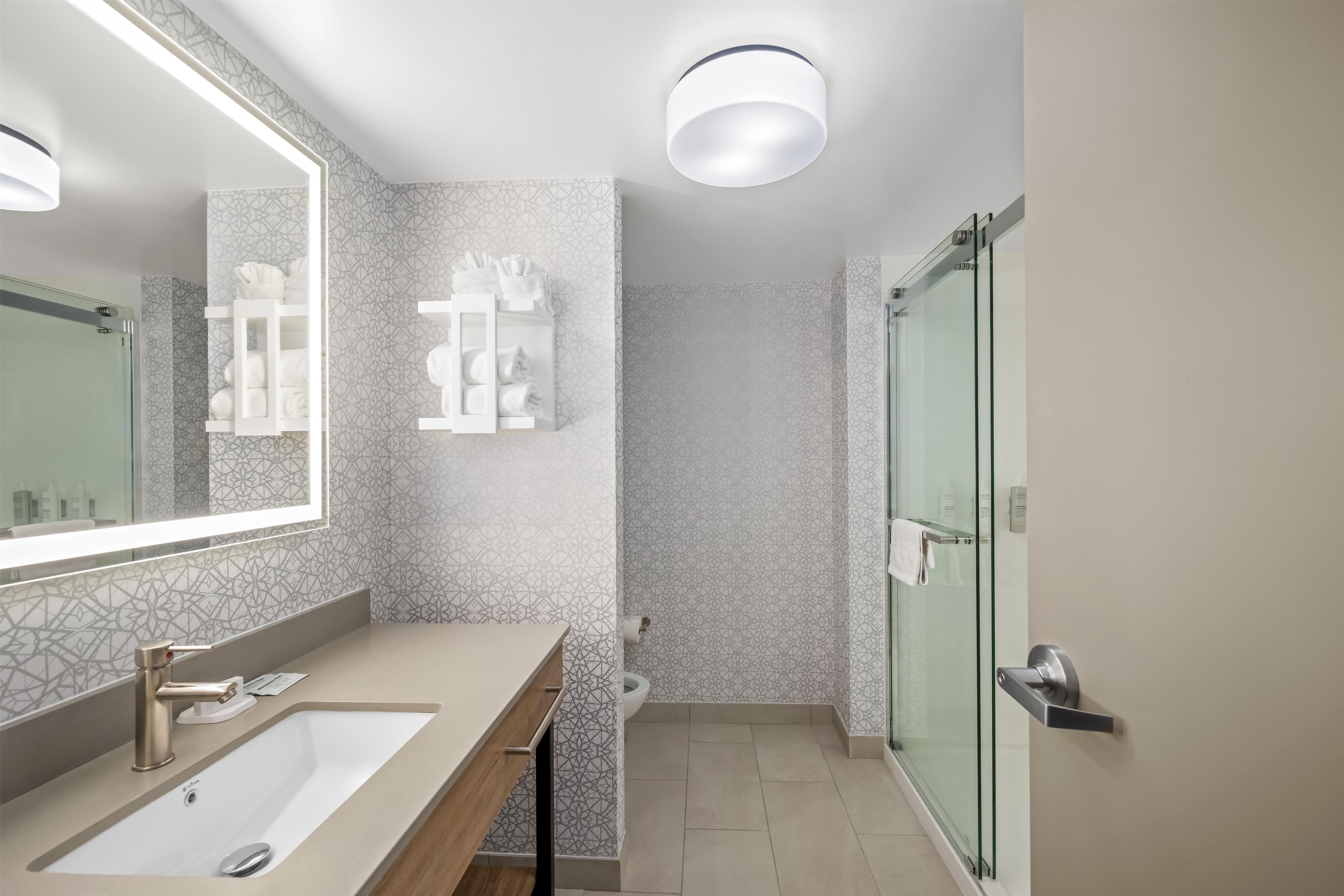 A modern bathroom with a large mirror, a sink, and a glass shower enclosure.