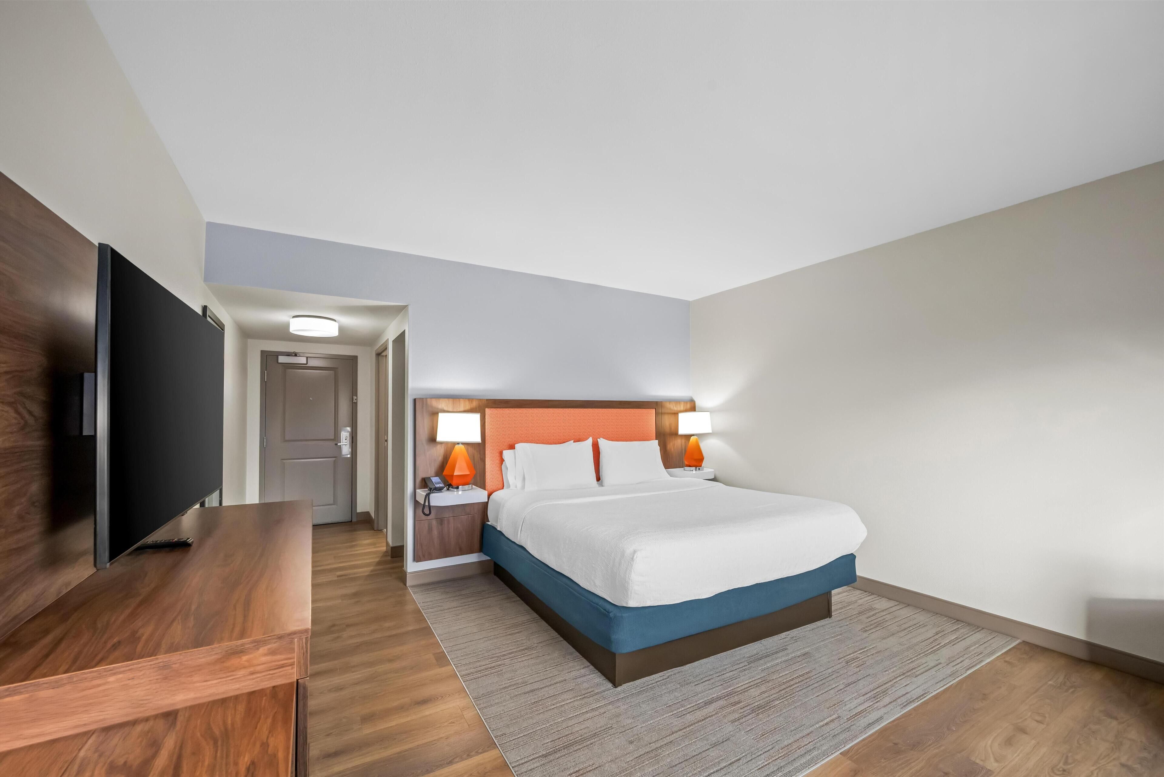 A hotel room with a bed, a TV, a desk, and a nightstand with lamps.