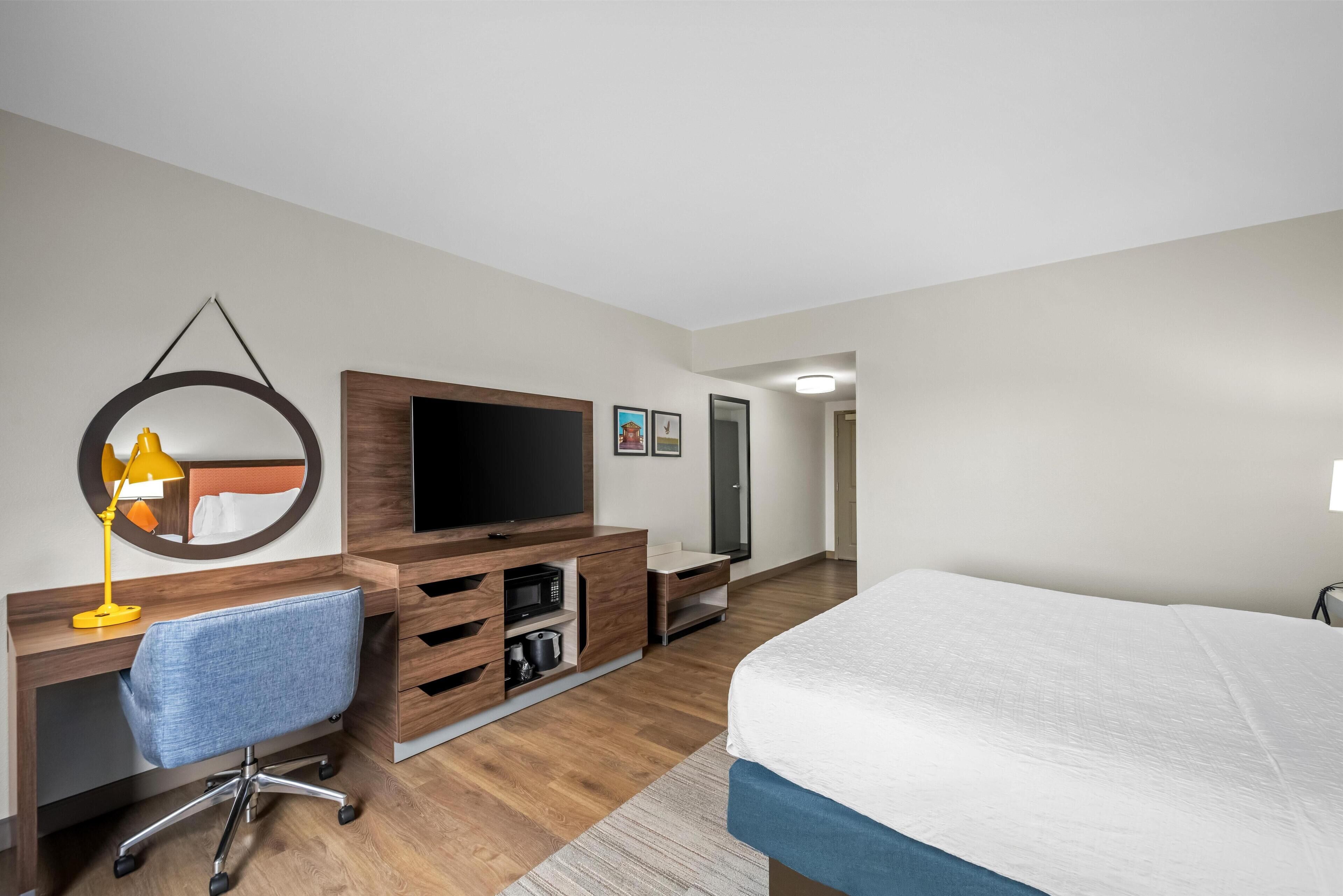 Une chambre d’hôtel moderne équipée d’un bureau en bois, d’une télévision, d’un lit et d’un miroir.