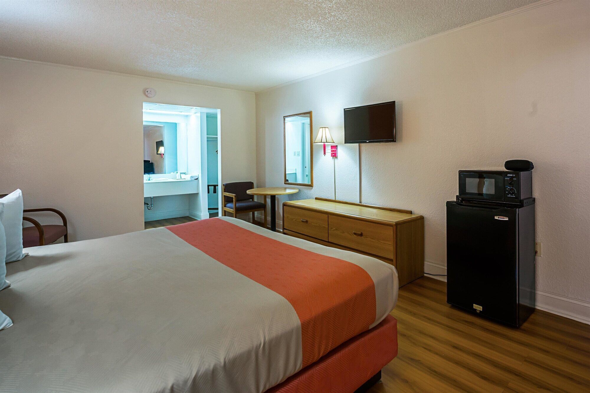 A hotel room with a bed, a dresser, a desk, a chair, a television, and a microwave.