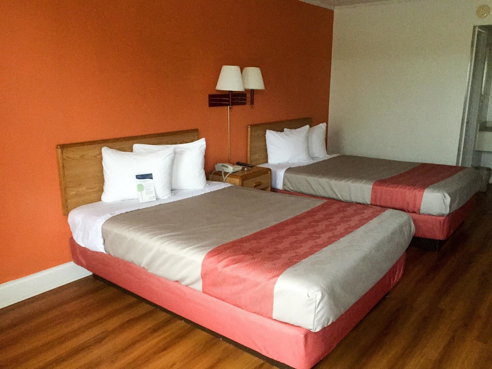 A hotel room with two beds, wooden headboards, and a nightstand with a lamp.