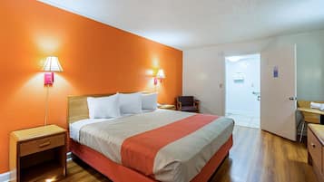 A hotel room with a bed, nightstands, a chair, and a door leading to a bathroom.