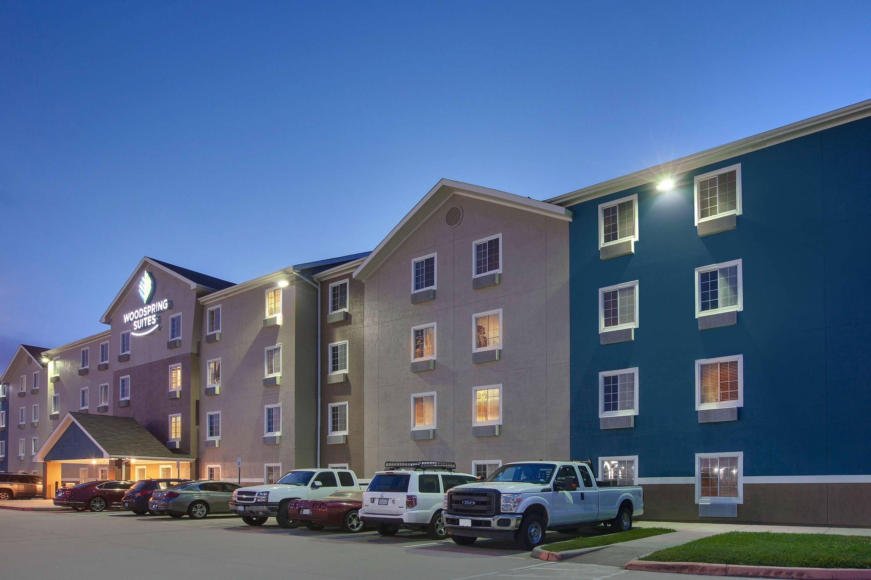 A hotel with multiple floors, a parking lot, and several vehicles parked.