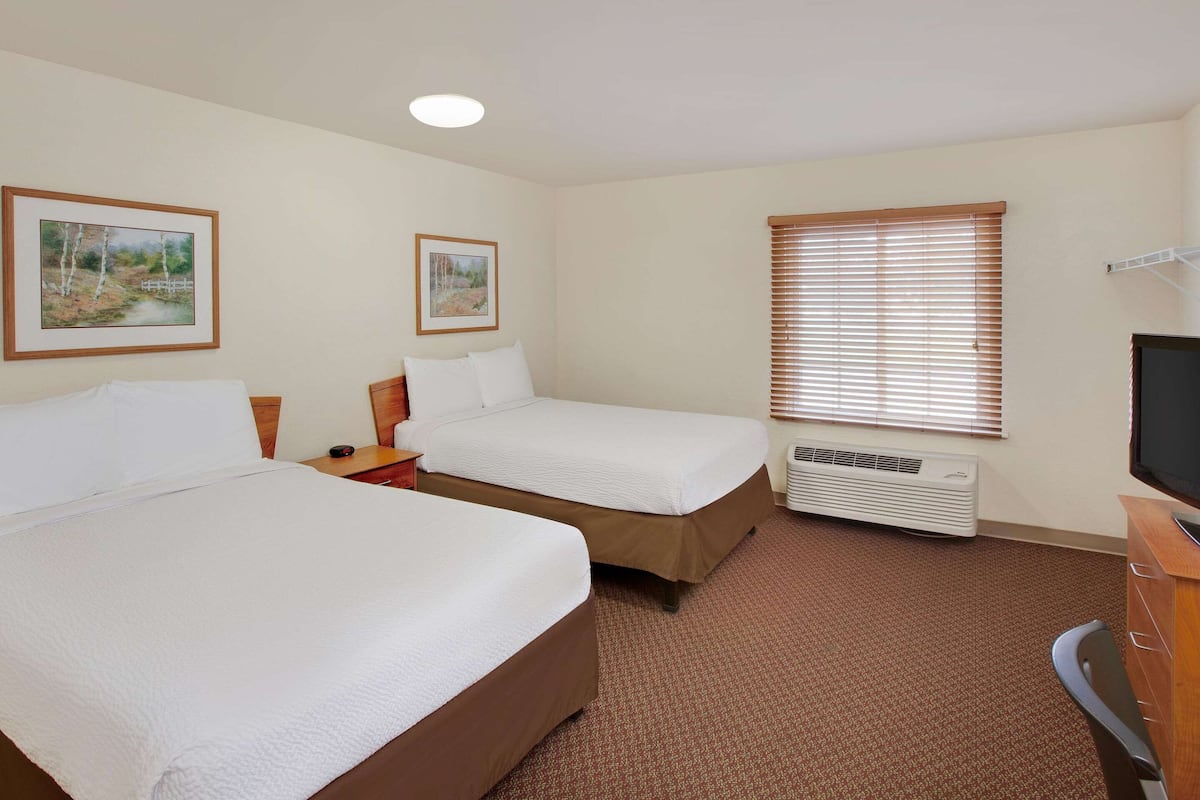 A hotel room with two beds, a television, a heater, and two framed pictures on the wall.