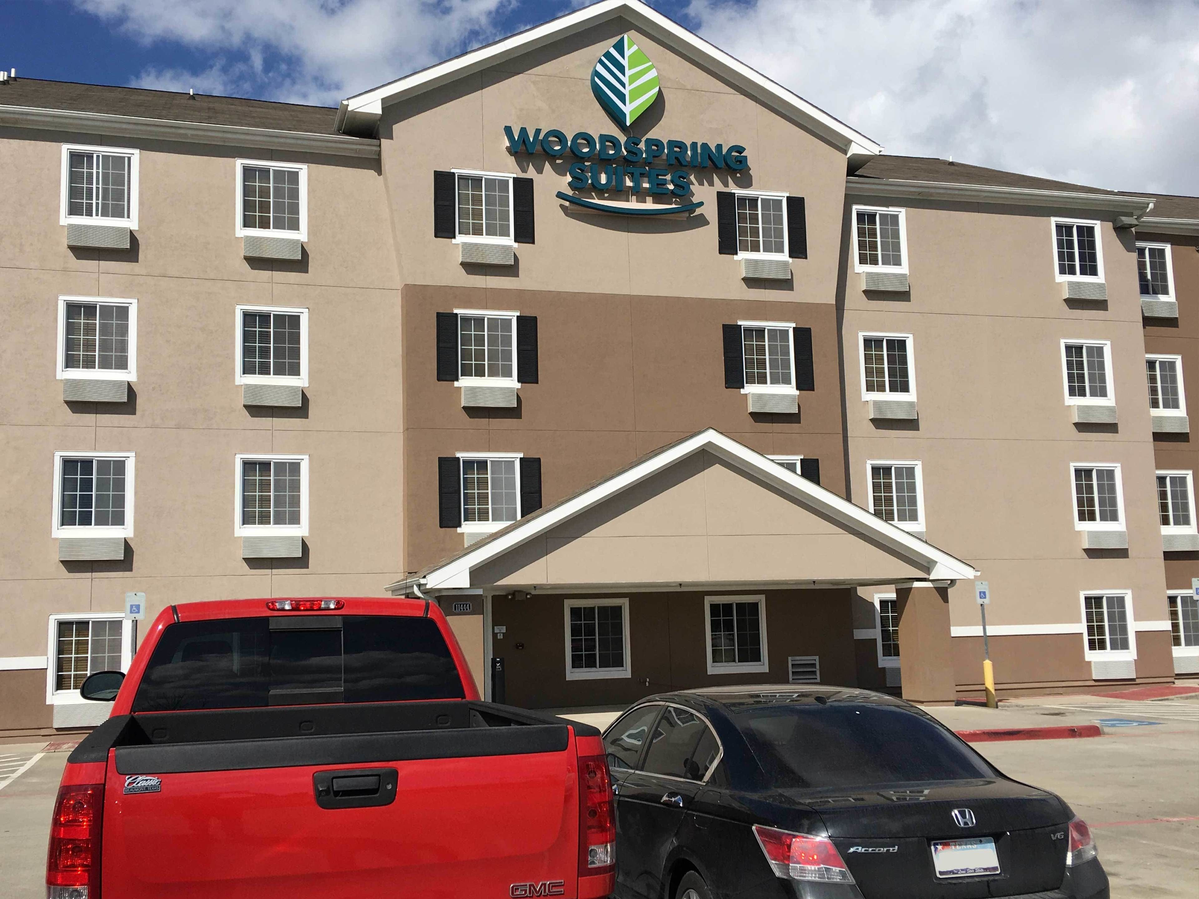 A multi-story hotel with a sign reading "Woodspring Suites". There are two vehicles parked in front.