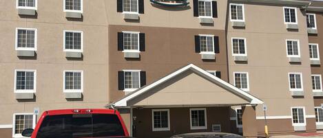 A multi-story hotel with a sign reading "Woodspring Suites". There are two vehicles parked in front.