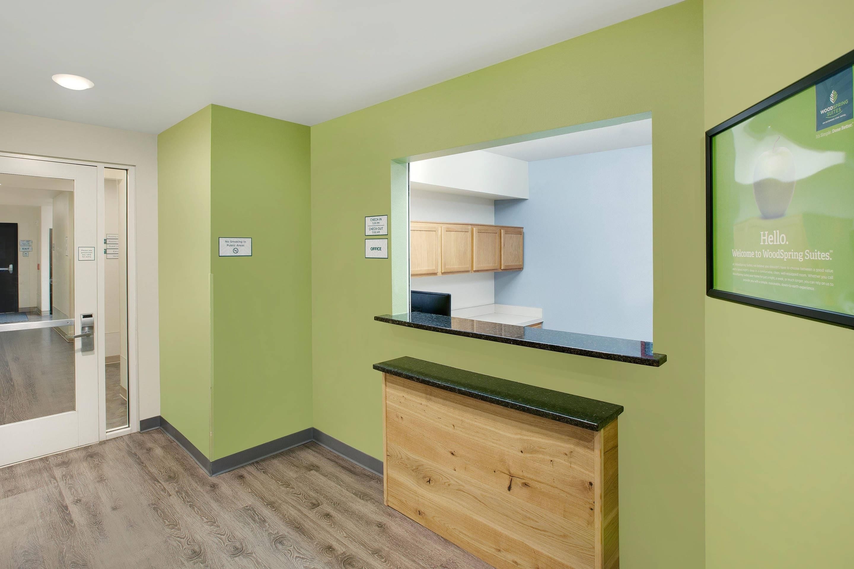 A reception area with a green wall, a wooden counter, and a check-in/out sign.