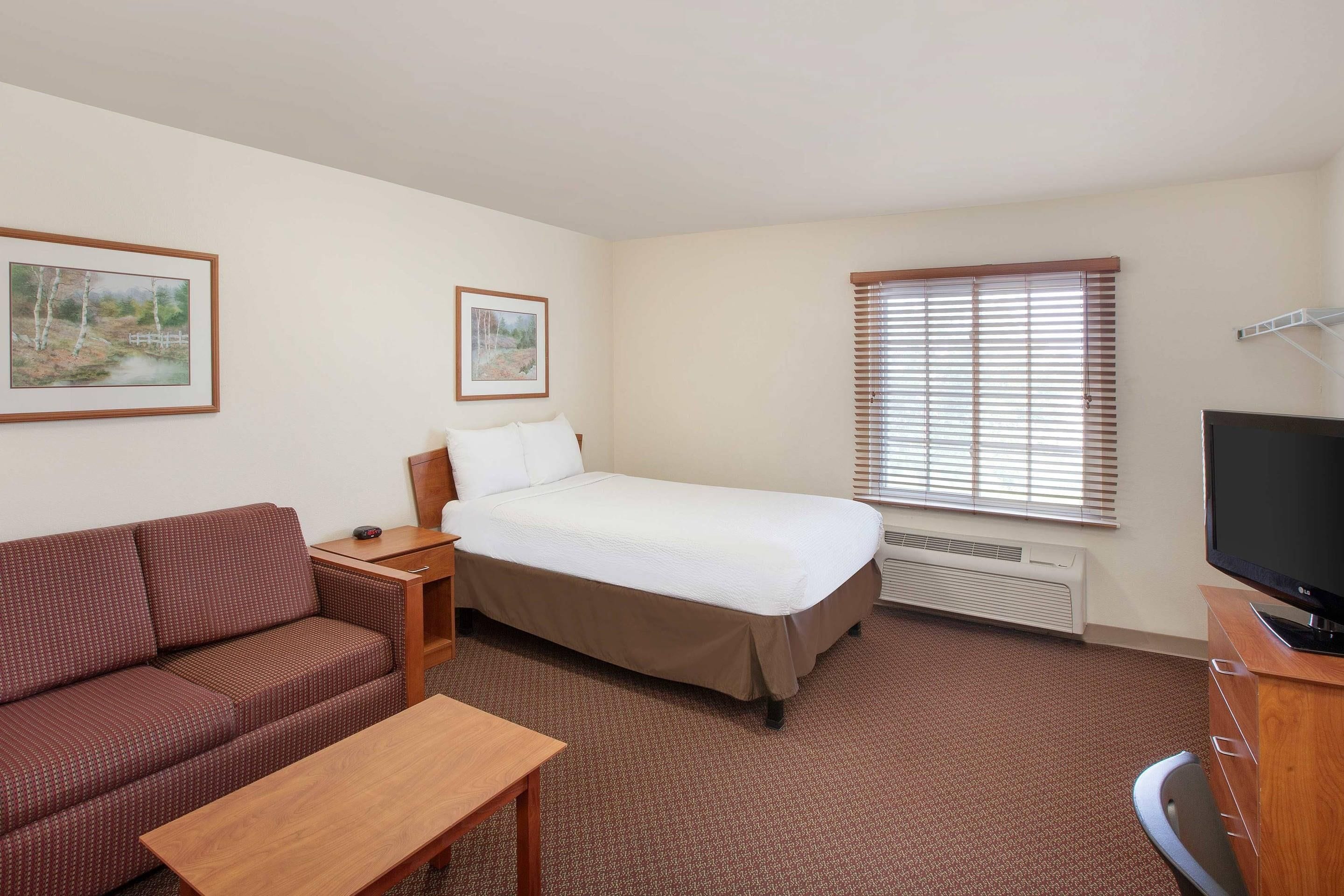 A hotel room with a bed, a sofa, a TV, and two framed pictures on the wall.