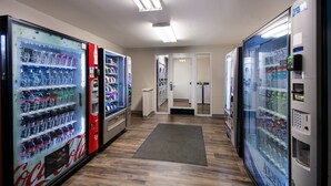 A hallway with vending machines, including Coca-Cola and Aquafina, and a laundry area in the background. - WoodSpring Suites Lexington (Lexington)