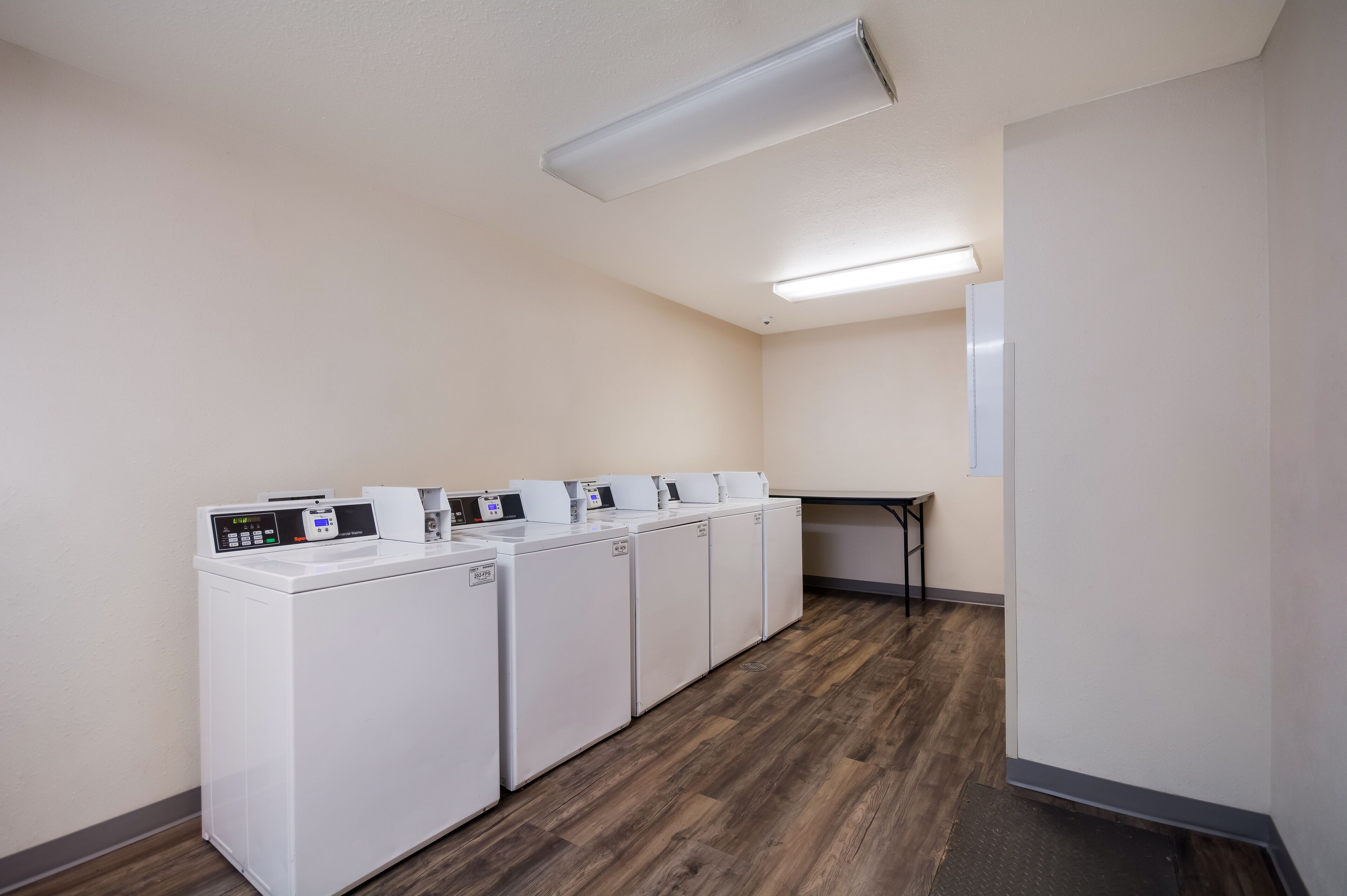 A laundry room with four white washing machines and a small table.