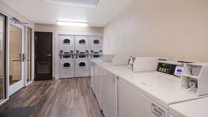 A laundry room with multiple washing machines and dryers, a digital control panel, and a door leading to another room. - WoodSpring Suites Lexington (Lexington)
