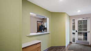 A hallway with a white reception desk, a computer on a shelf, and a door with a glass panel. - WoodSpring Suites Lexington (Lexington)