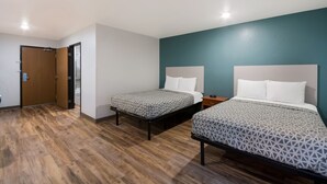A room with two beds, a wooden floor, a teal accent wall, and a door. - WoodSpring Suites Lexington (Lexington)