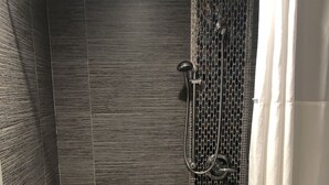 A shower area with a grab bar, a bench, and a tiled floor. - American Inn (Downey)