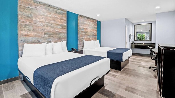 Hotellihuone, jossa on kaksi sänkyä, työpöytä ja suuri peili.