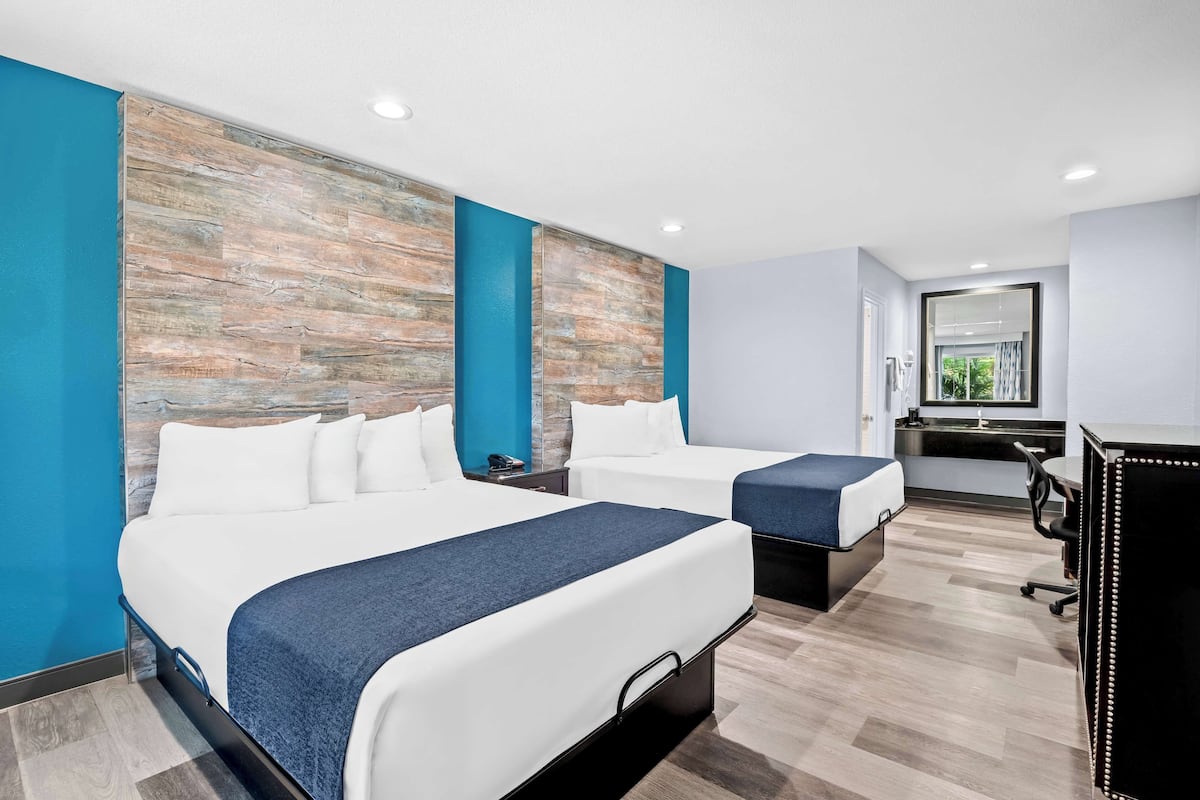 A hotel room with two beds, a desk, and a large mirror.