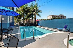 A swimming pool area with blue umbrellas, lounge chairs, and a palm tree backdrop. - SureStay Hotel by Best Western Buena Park Anaheim (Buena Park)