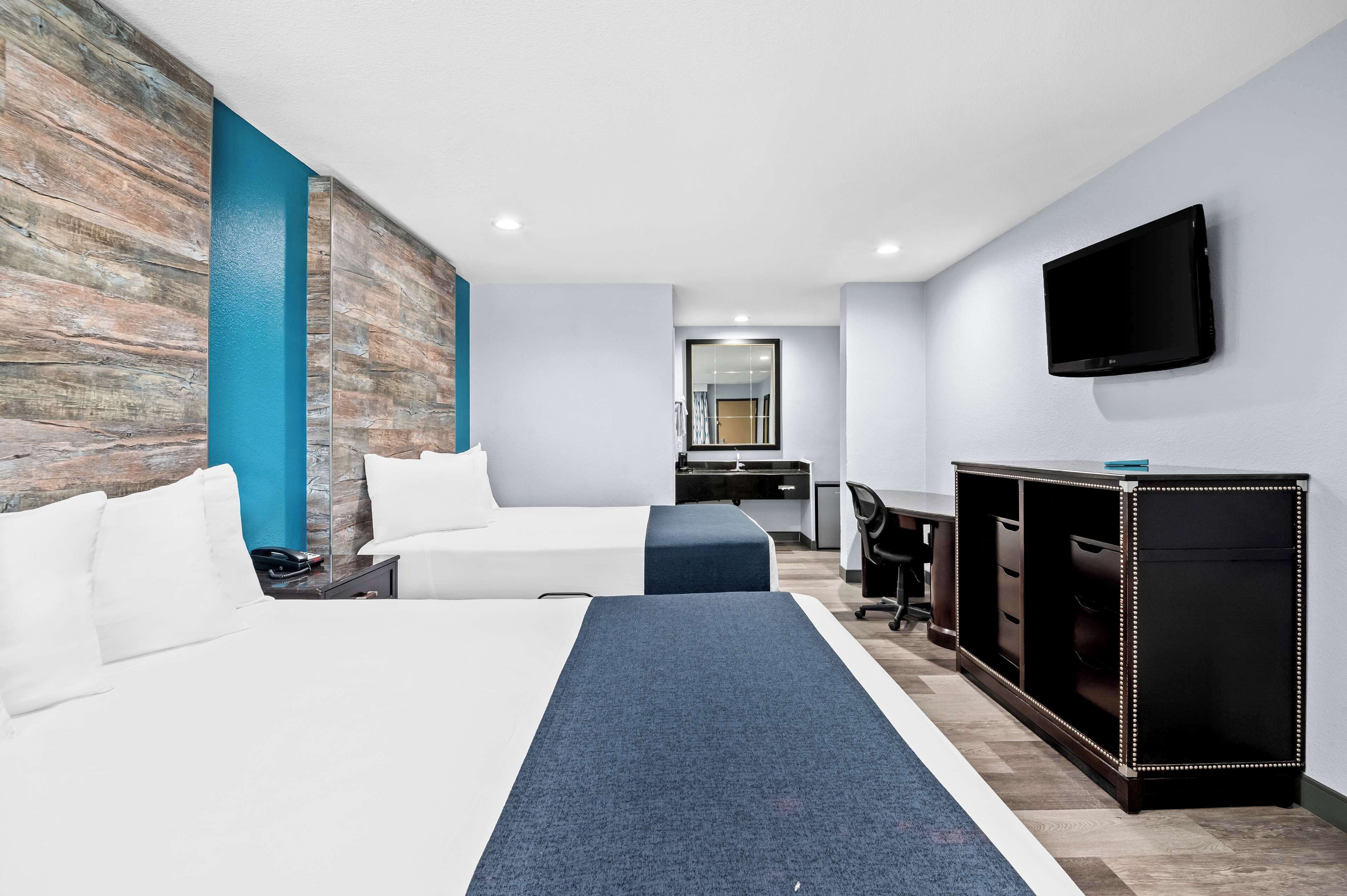 Una habitación de hotel con dos camas, un escritorio, una silla, un televisor y un armario.