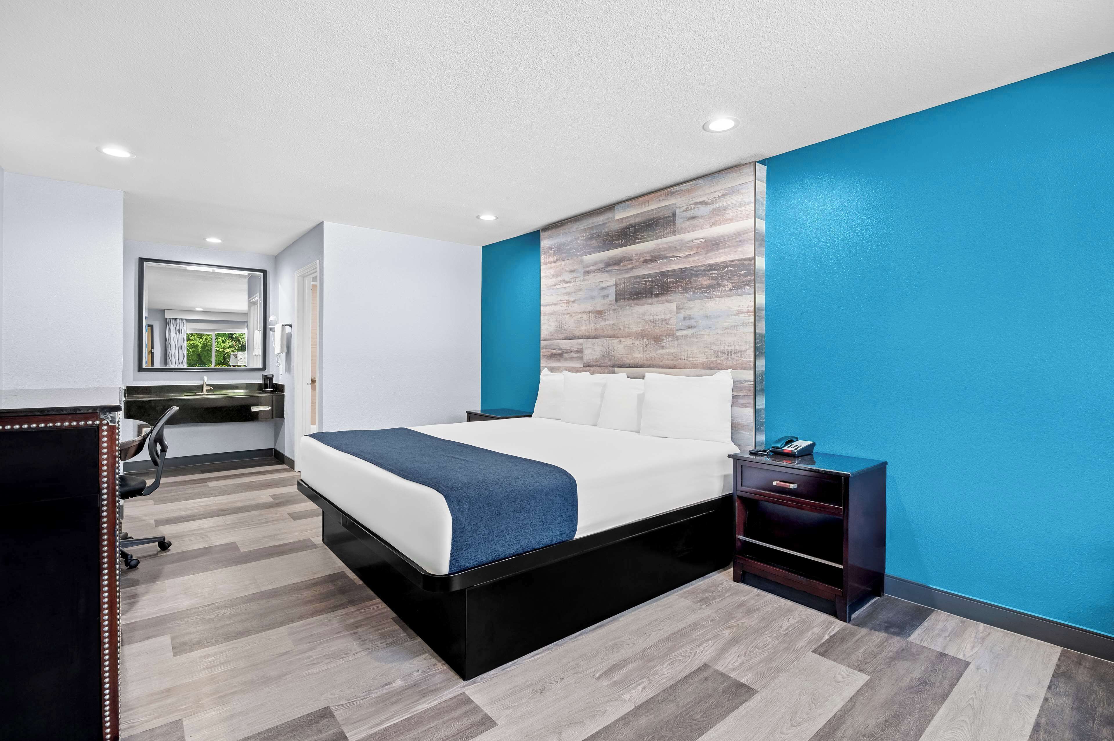 A modern hotel room with a large bed, a desk, and a mirror.