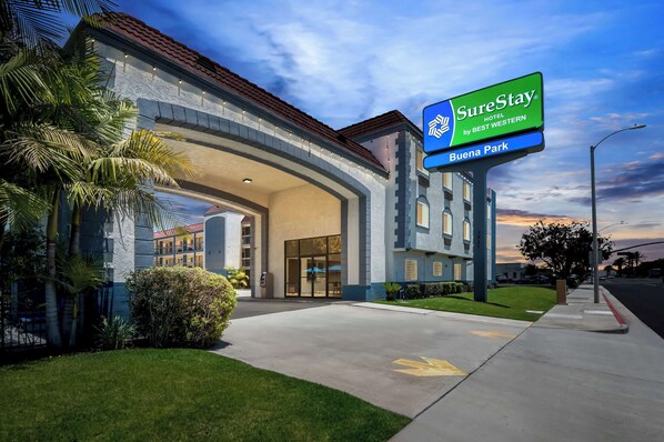 A SureStay hotel entrance with a clear sky, palm trees, and a well-maintained lawn. - SureStay Hotel by Best Western Buena Park Anaheim (Buena Park)