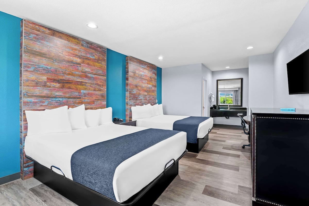 A hotel room with two beds, a desk, a TV, and a bathroom visible through an open door.