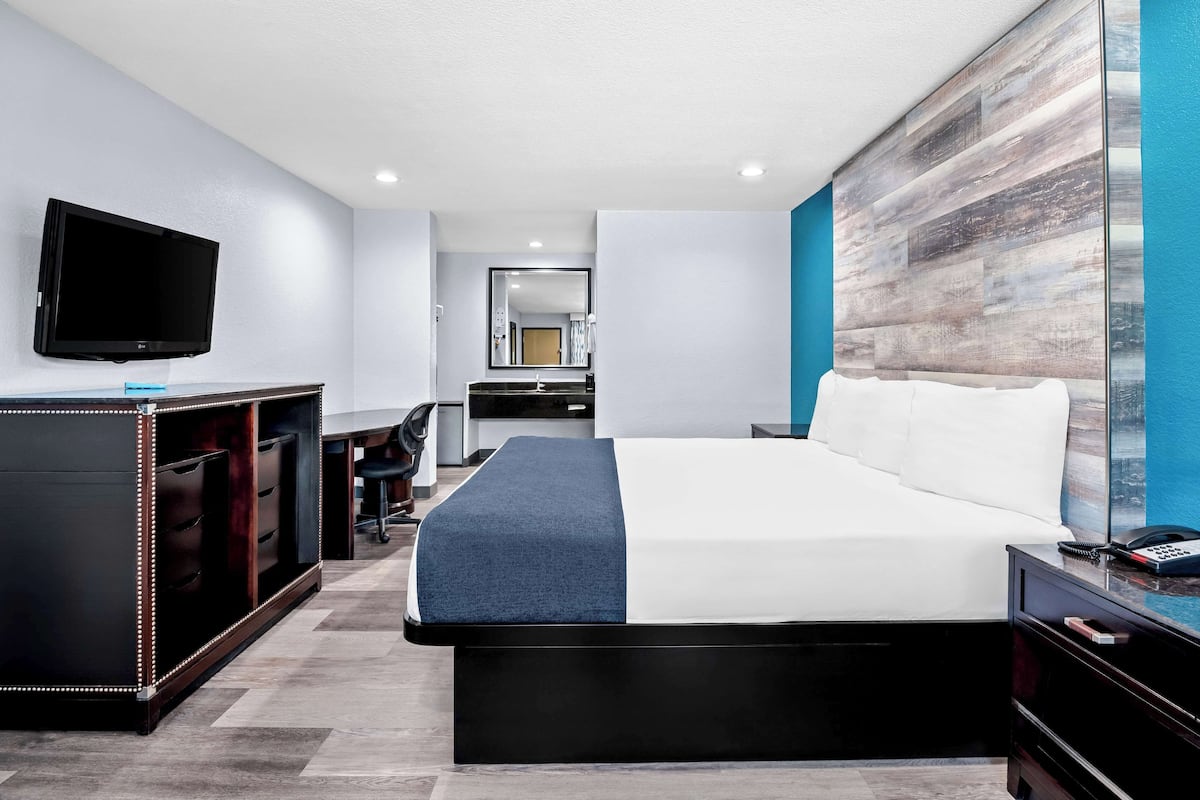 A modern hotel room with a large bed, a flat-screen TV, a desk with a chair, and a large mirror.