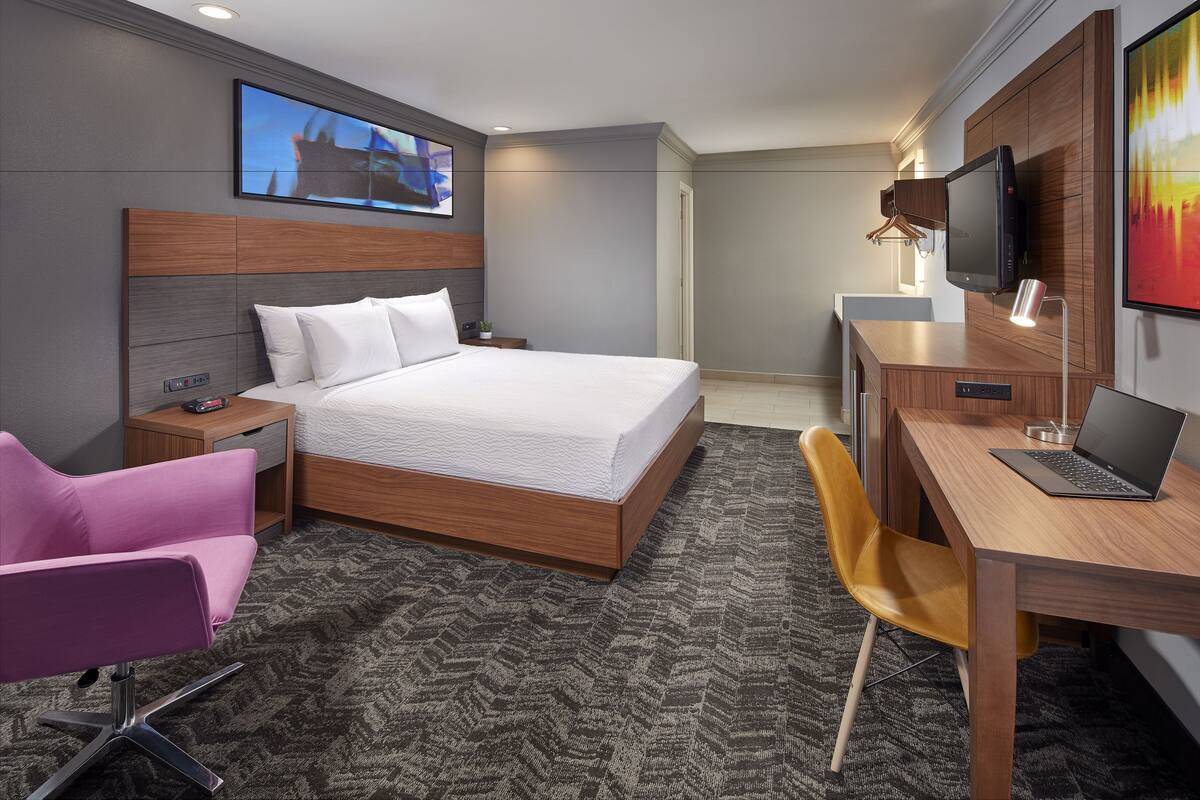 Una habitación de hotel moderna con una cama grande, un escritorio con una computadora portátil, un televisor y una silla.