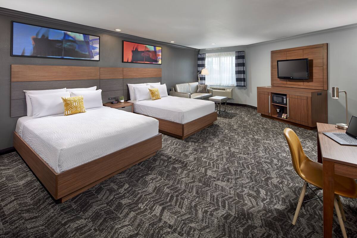 Habitación de hotel con dos camas, un escritorio, un televisor y una zona de estar.