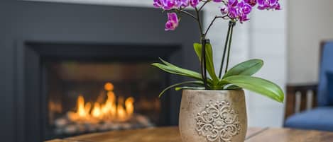 A potted orchid on a wooden table with a fireplace in the background.