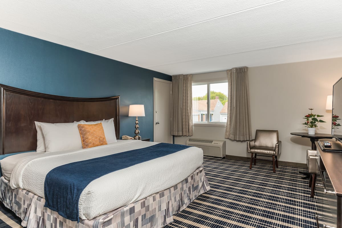 A hotel room with a large bed, a desk, a chair, and a window with curtains.