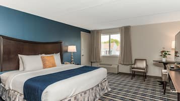 A hotel room with a large bed, a desk, a chair, and a window with curtains.