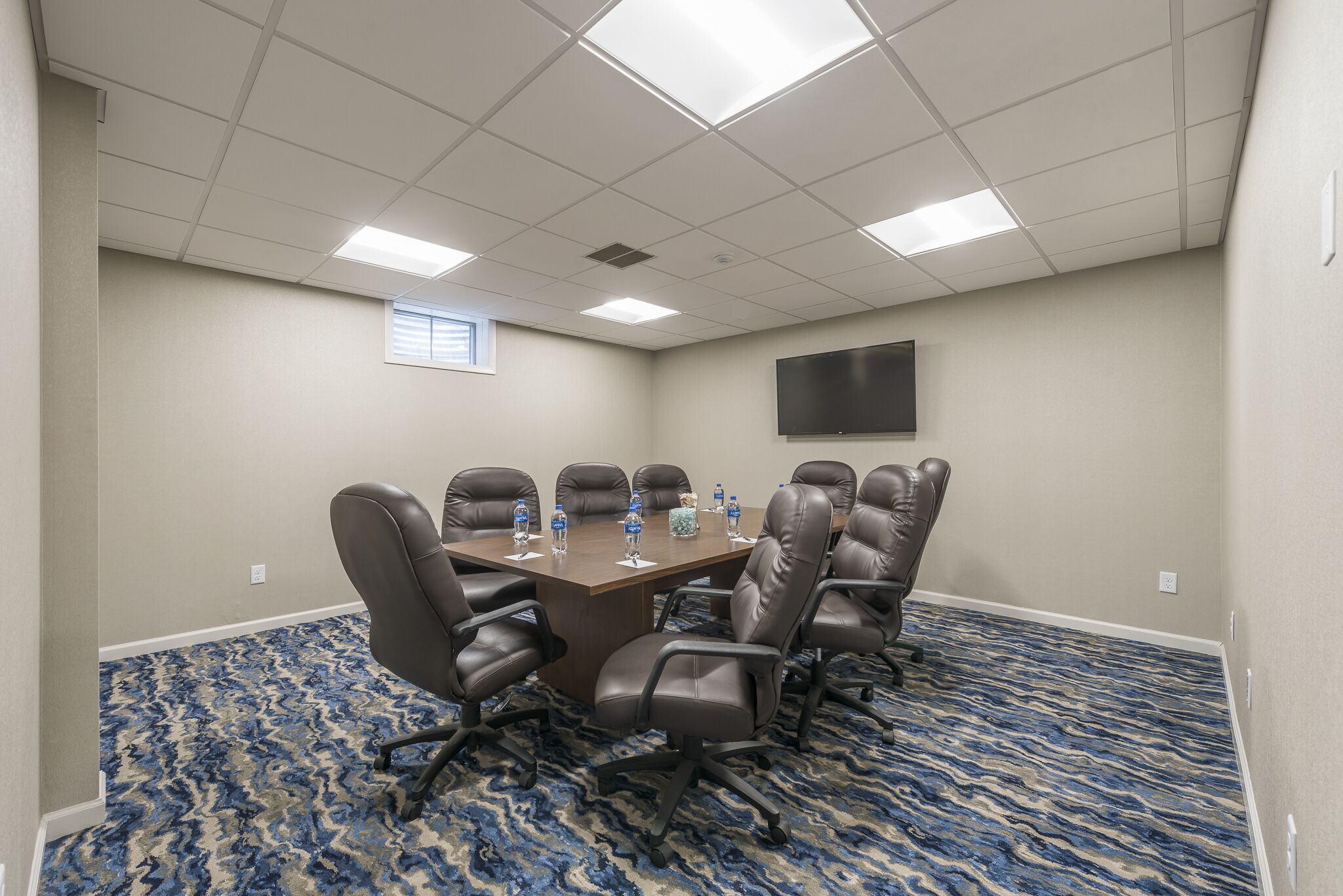 A conference room with a large table, six chairs, and a flat-screen TV on the wall.