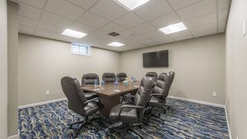 A conference room with a large table, six chairs, and a flat-screen TV on the wall.