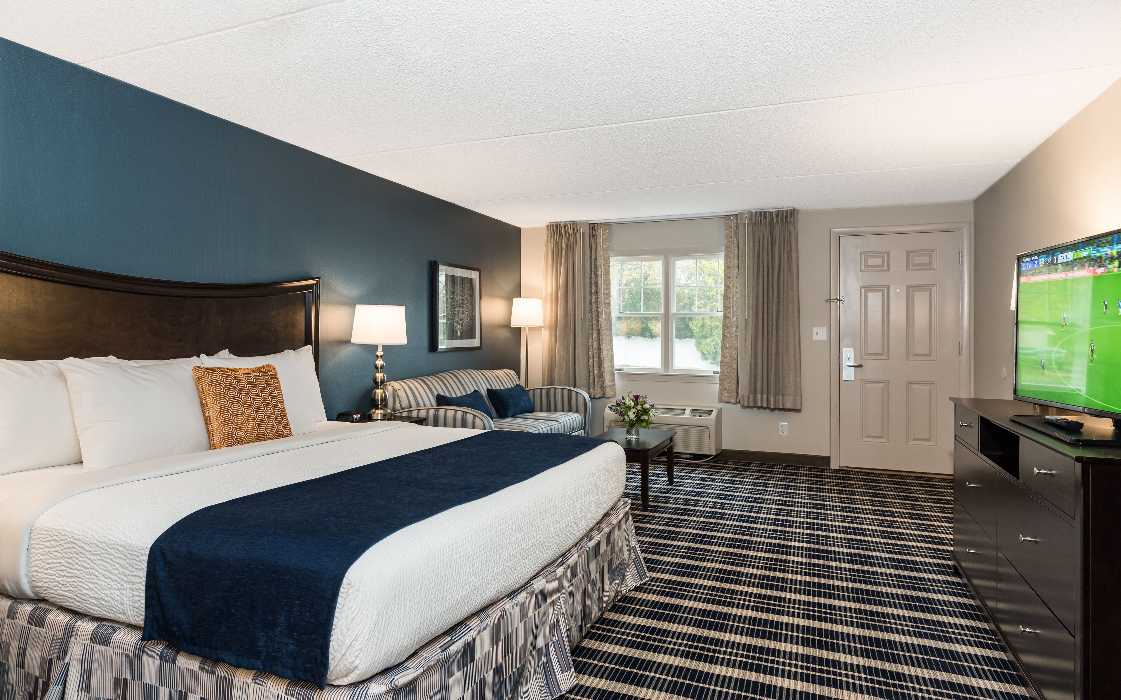 A hotel room with a large bed, a sofa, a TV, and a window with curtains.