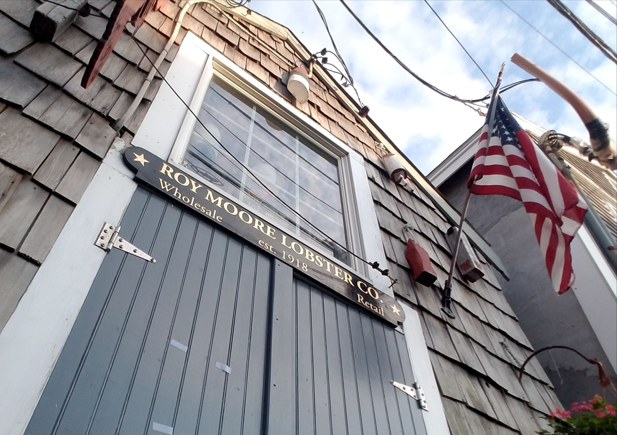 Una fachada con un letrero que dice "ROY MOORE LOBSTER CO. Retail" y una bandera estadounidense.