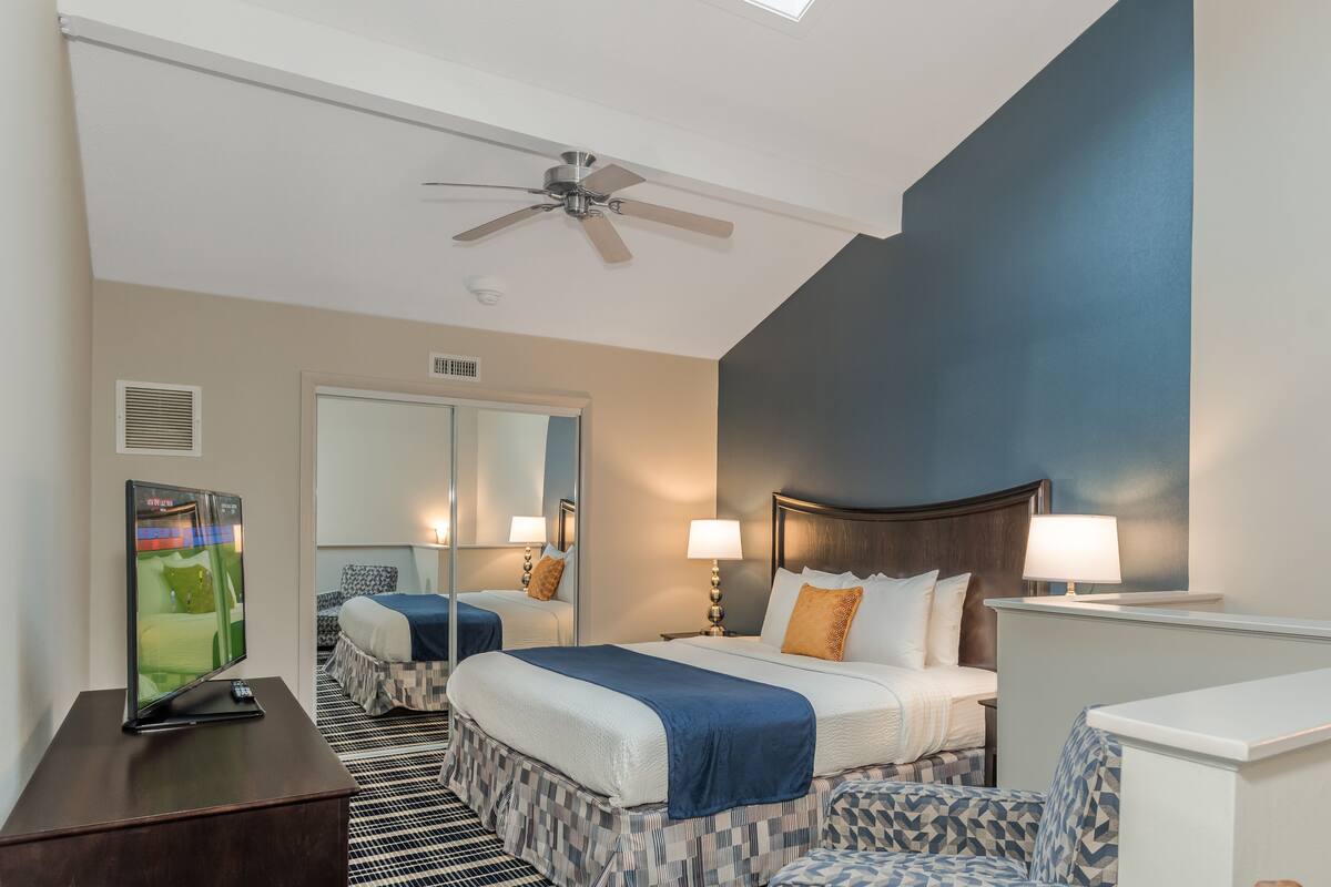 A hotel room with two beds, a ceiling fan, a television, and a patterned rug.