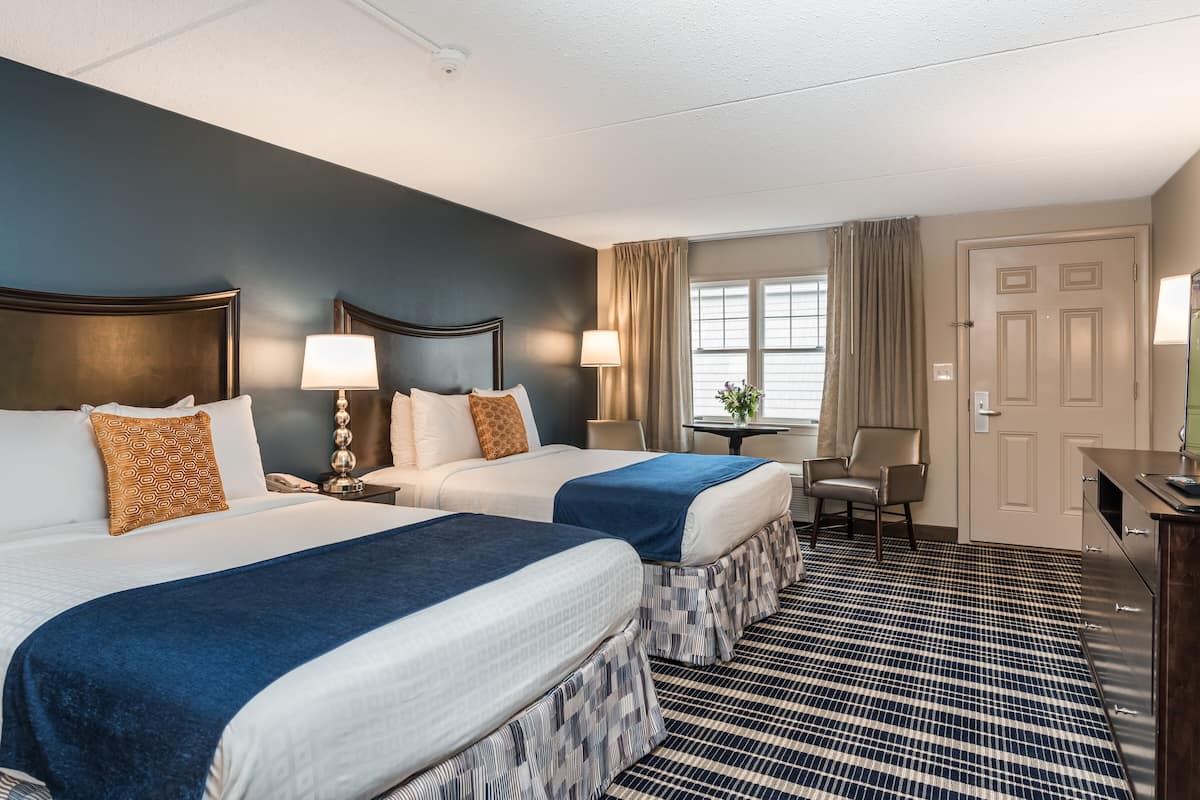 A hotel room with two beds, a desk, and a chair.