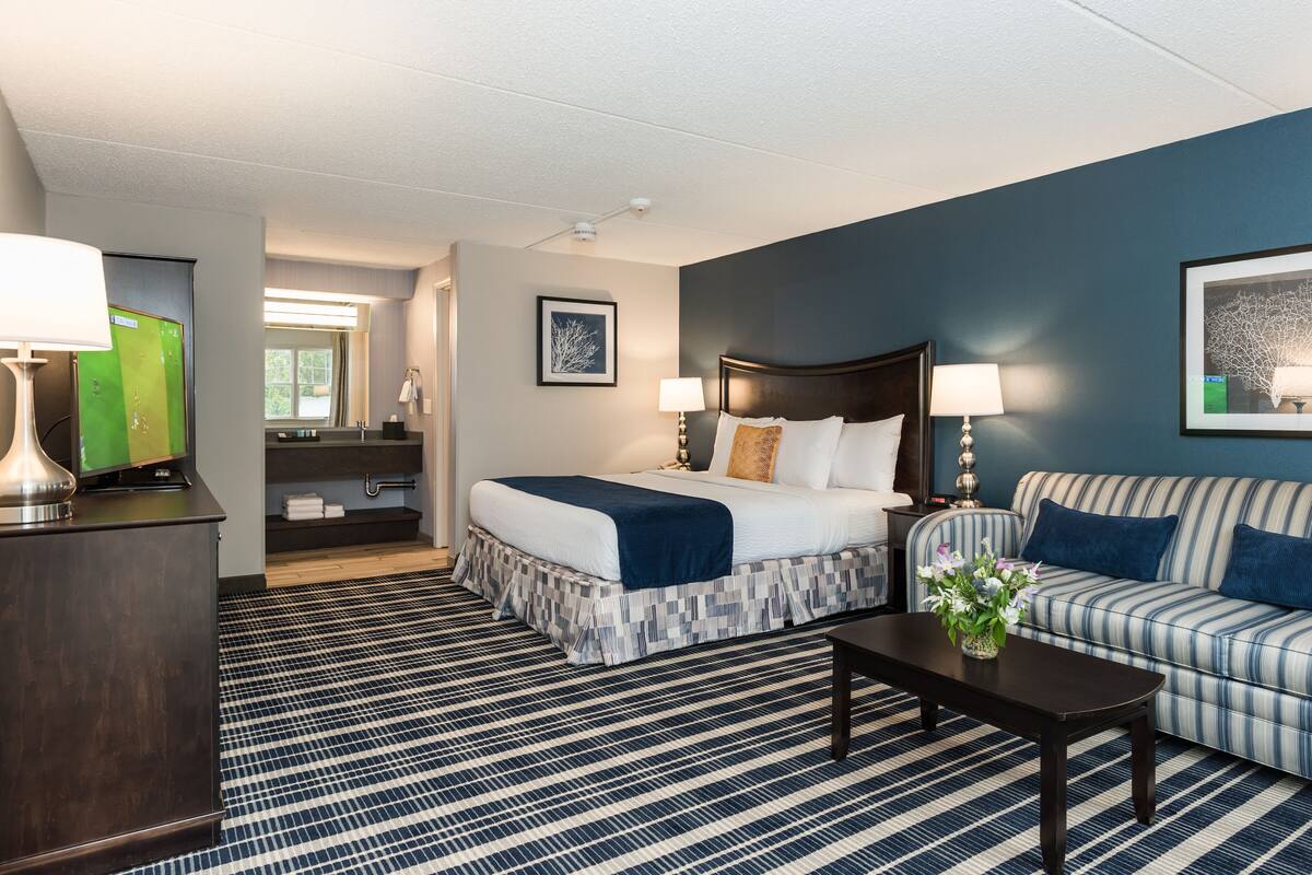 A hotel room with a bed, a sofa, a coffee table, a TV, and a bathroom visible through an open door.