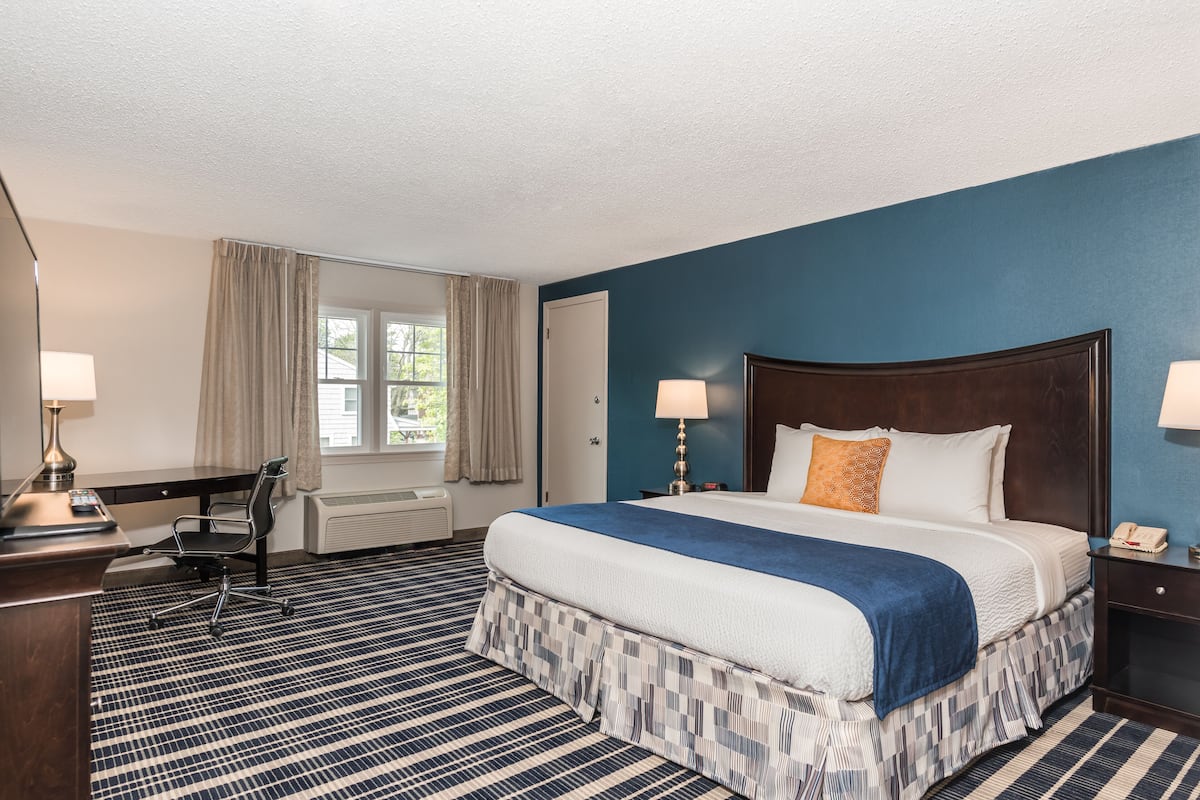 A hotel room with a large bed, a desk, a chair, and a window with curtains.