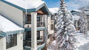 Un immeuble à plusieurs étages doté de balcons, entouré d’arbres couverts de neige.