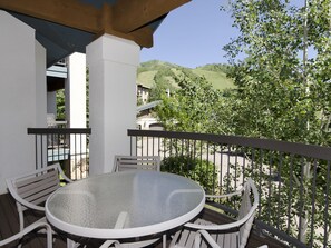 A covered outdoor seating area with a round table and chairs, overlooking a hilly landscape with trees and buildings. - The Trails at Storm Meadows by Mountain Resorts (Steamboat Springs)